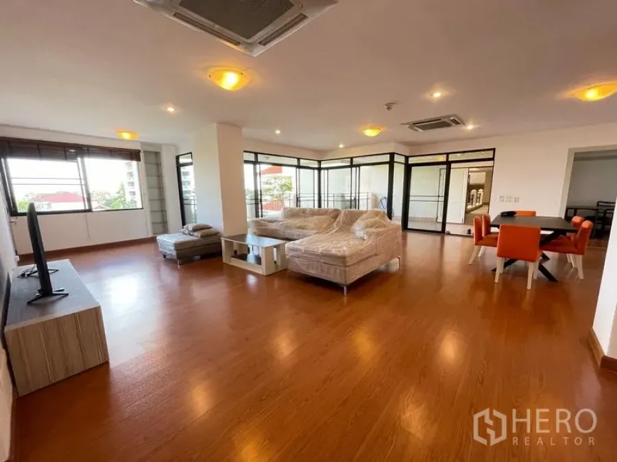 Condominium for rent in Watthana, Bangkok - Spacious open-plan living and dining area with wood floors, sofa set and wide windows in an Ekkamai condo.