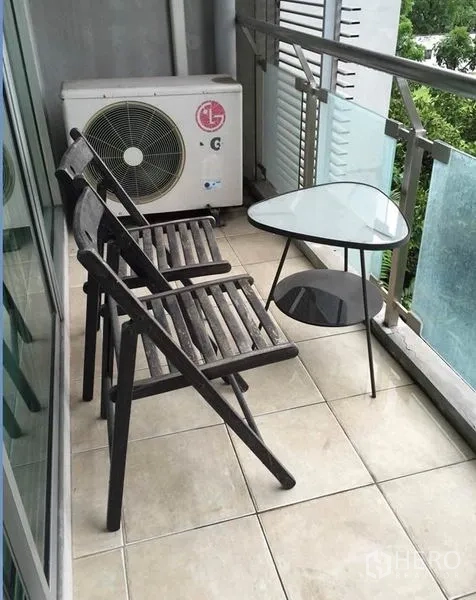 คอนโด ให้เช่าในKhlong Toei, Bangkok - ระเบียงแคบมีเก้าอี้ไม้สองตัว โต๊ะกระจก ราวกันตกกระจก และวิวต้นไม้