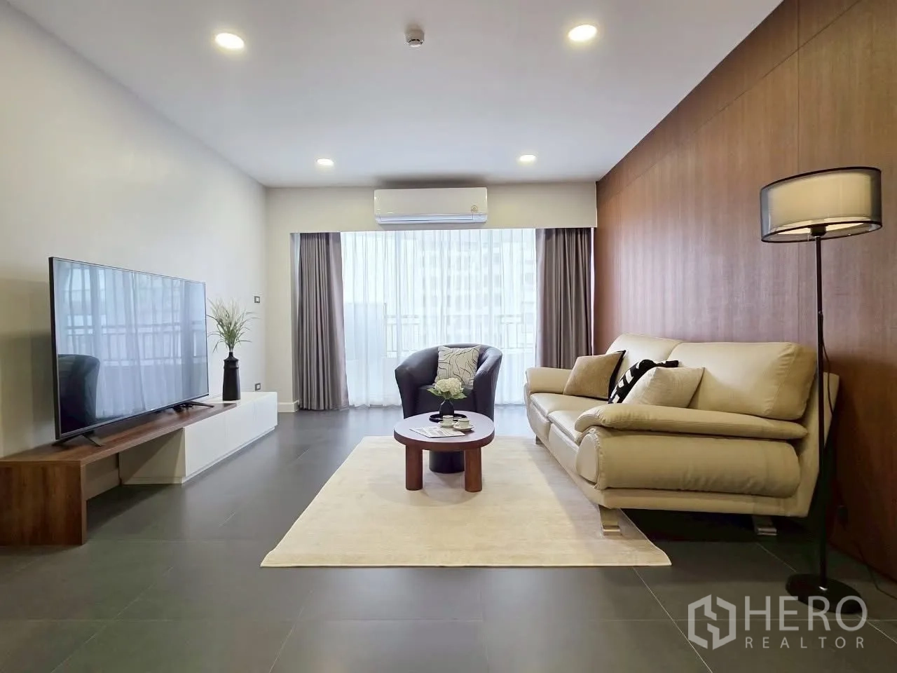 Condominium for rent in Sathon, Bangkok - Modern living room with sofa, armchair and TV opening to the balcony.