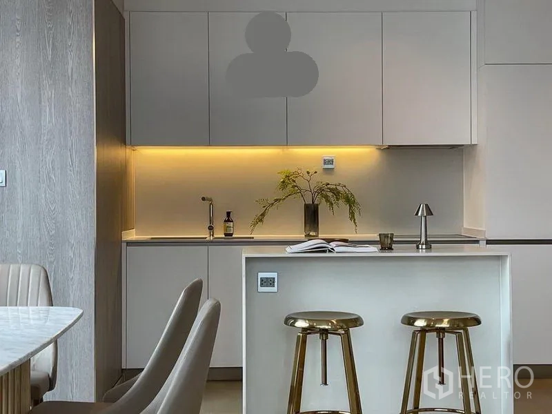 公寓 出租在Watthana, Bangkok - 现代一体化厨房，白色橱柜、灯带照明与大理石岛台配金色吧椅。