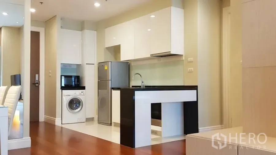 公寓 出租在Khlong Toei, Bangkok - 现代开放式厨房，白色橱柜与黑色中岛台面，配冰箱与洗衣机，木地板。