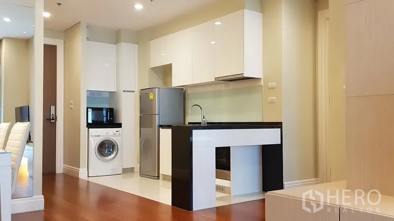 公寓 出租在Khlong Toei, Bangkok - 现代开放式厨房，白色橱柜与黑色中岛台面，配冰箱与洗衣机，木地板。
