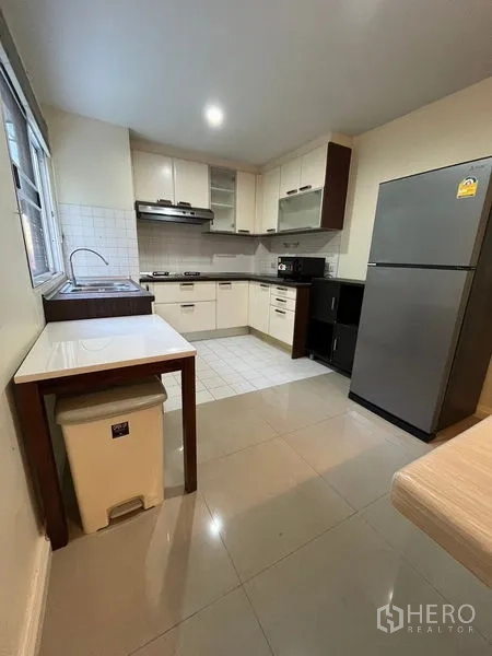 Townhouse for rent in Phaya Thai, Bangkok - L-shaped kitchen with white cabinetry, gas hob, range hood, sink and window for natural light.