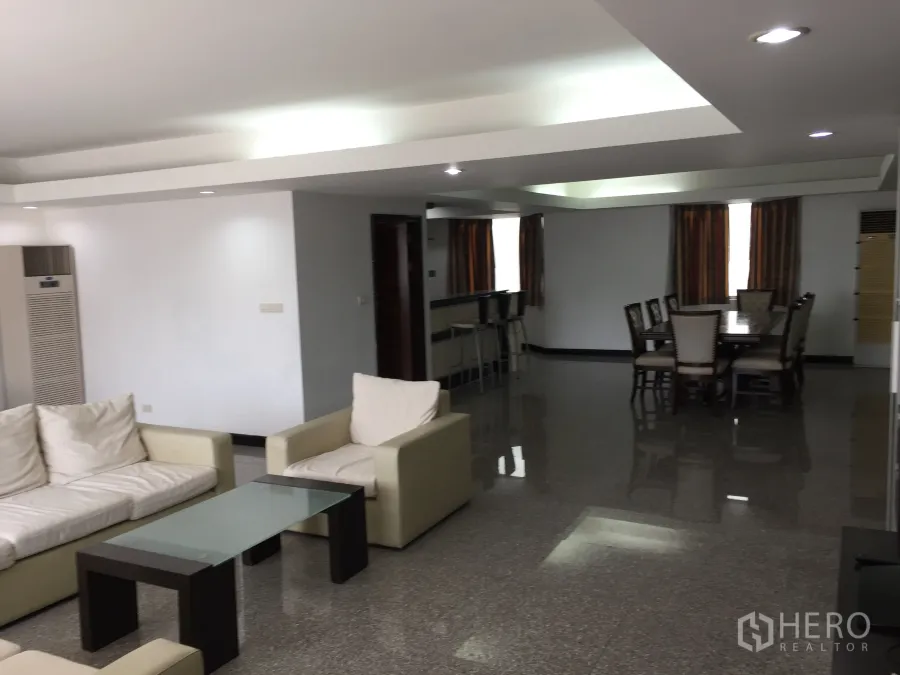 Condominium for rent in Watthana, Bangkok - Open-plan living and dining area with cream sofas, glass coffee table, recessed lighting, and glossy floors.