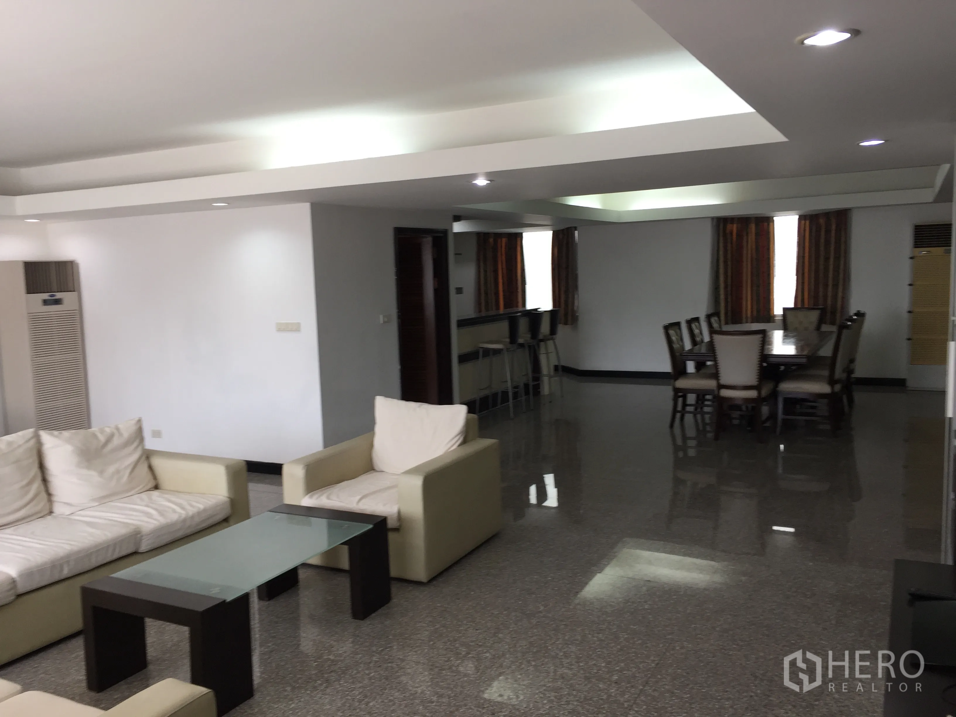 Condominium for rent in Watthana, Bangkok - Open-plan living and dining area with cream sofas, glass coffee table, recessed lighting, and glossy floors.