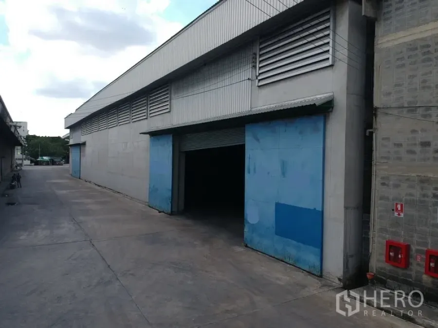 工厂 出租在Phra Pradaeng, Samut Prakan - 大型工业仓厂外观，蓝色推拉门与通风百叶，宽阔车道可通行卡车。