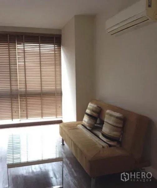 คอนโด ให้เช่าในKhlong Toei, Bangkok - พื้นที่นั่งเล่นอบอุ่น โซฟาสีแทน แอร์ โต๊ะกลางกระจก และมู่ลี่หน้าต่างบานใหญ่