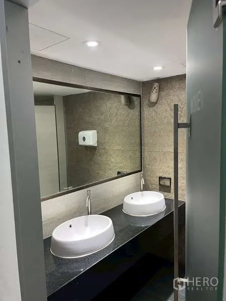 Office Space for rent - Restroom with double vessel sinks, a large mirror, and modern lighting.