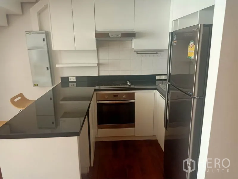 Condominium for rent in Watthana, Bangkok - Close-up of the kitchen showing built-in oven, cooktop, range hood, and stainless-steel refrigerator.