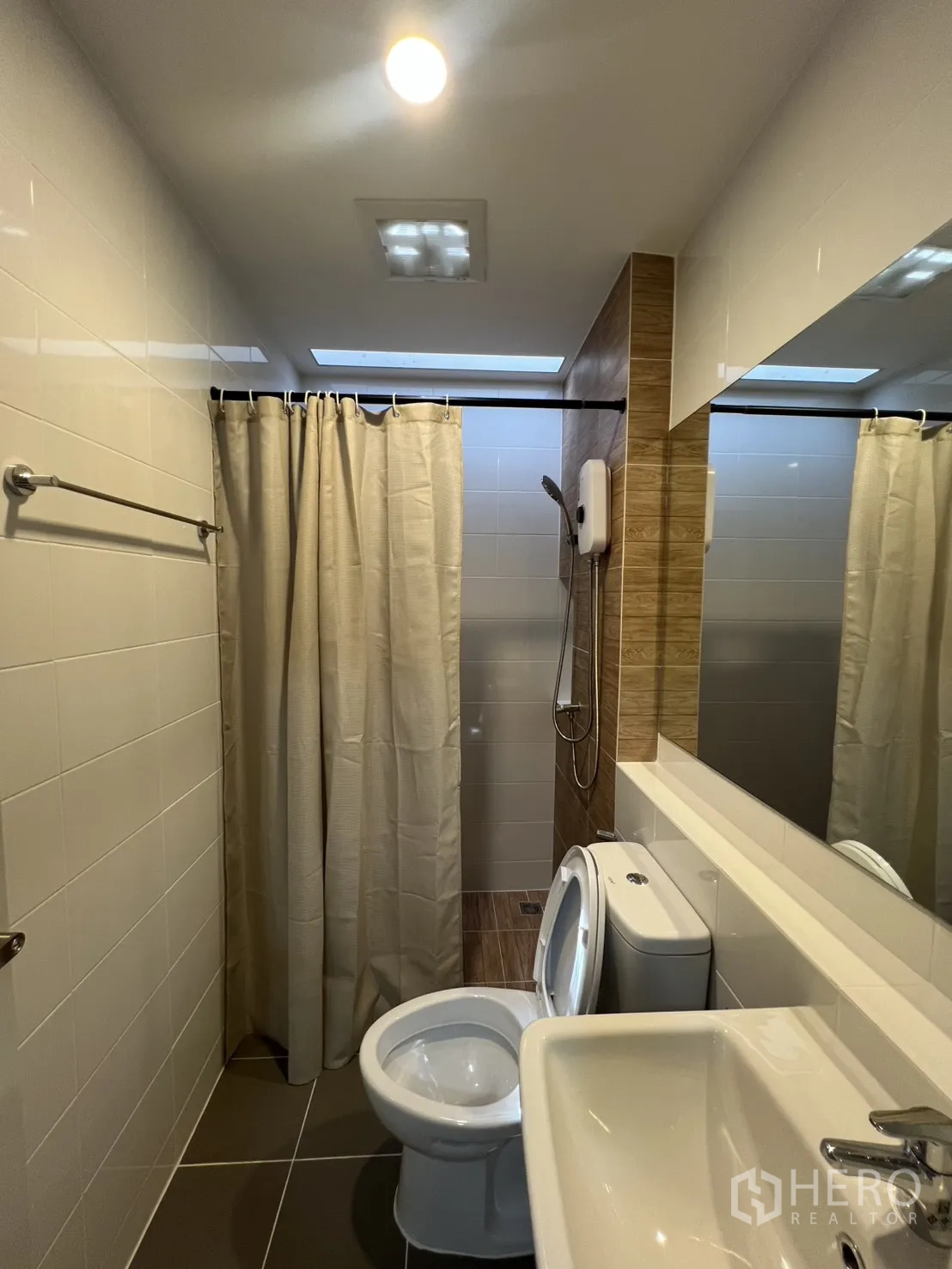 Townhouse for rent in Bang Phli, Samut Prakan - Bathroom with shower behind a curtain, toilet and sink with mirror.