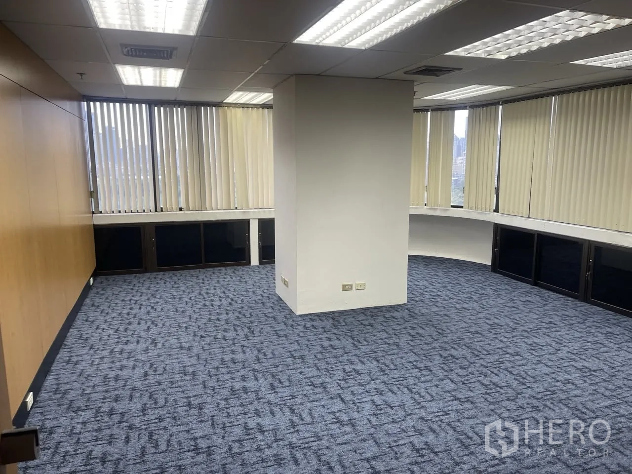 Office Space for rent in Khlong Toei, Bangkok - Open-plan workspace with wood-paneled wall, central column, and fluorescent grid lighting.