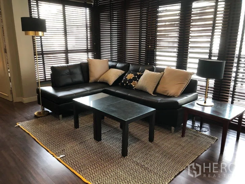 คอนโด ให้เช่าในKhlong Toei, Bangkok - มุมนั่งเล่นสว่างด้วยโซฟาหนังสีดำ โต๊ะกลาง และพรมลายก้างปลาใกล้หน้าต่างเต็มบาน