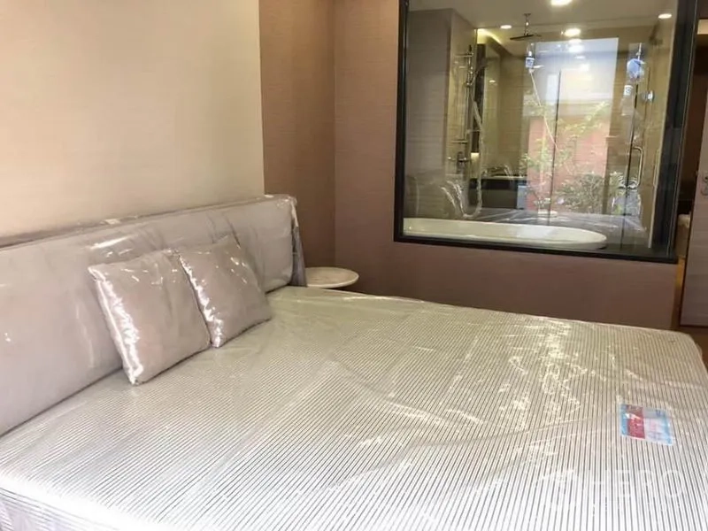 Condominium for rent in Pathum Wan, Bangkok - Bedroom with large bed and glass window looking into bathroom with tub and shower.