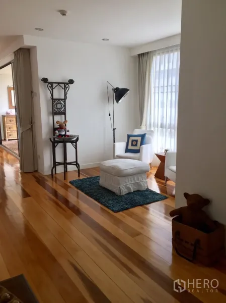 Condominium for rent in Watthana, Bangkok - Cozy reading nook by floor-to-ceiling windows with armchair, ottoman, floor lamp and blue rug.