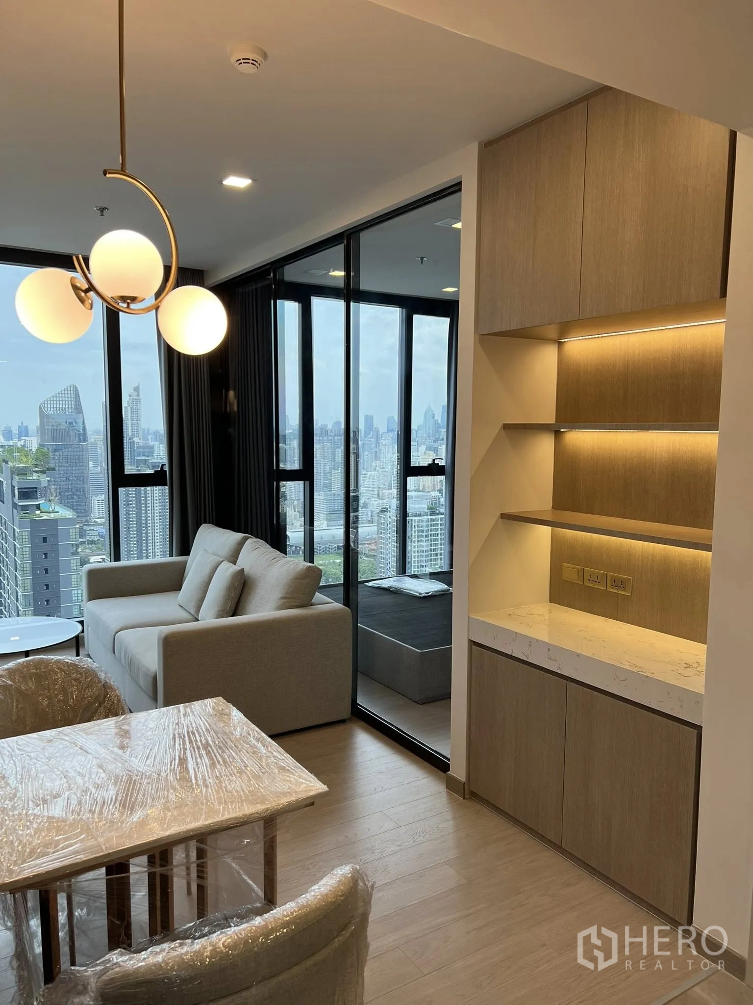 公寓 for rent in Huai Khwang, Bangkok - 带灯内嵌式置物柜、沙发及玻璃卧室隔断，窗外为开阔城市景观。