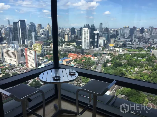 Condominium for rent or sale in Ratchathewi, Bangkok - Corner balcony with bistro table and stools offering sweeping skyline panoramas.