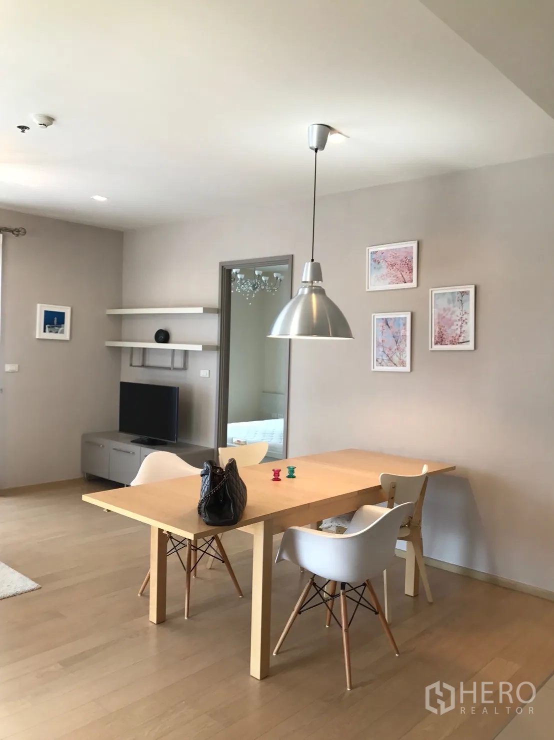 Condominium for rent or sale in Watthana, Bangkok - Bright dining area with wooden table, white chairs and a pendant light next to the TV corner.