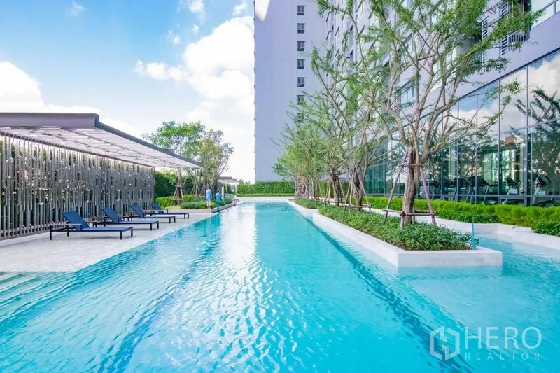 Condominium for rent in Phra Khanong, Bangkok - Long lap pool with sun loungers, trees and a glass-walled fitness pavilion.