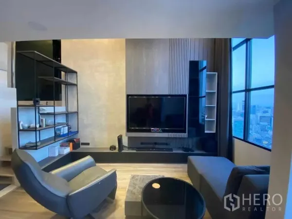 Condominium for rent or sale in Sathon, Bangkok - TV feature wall and seating area beside tall windows with panoramic city views.