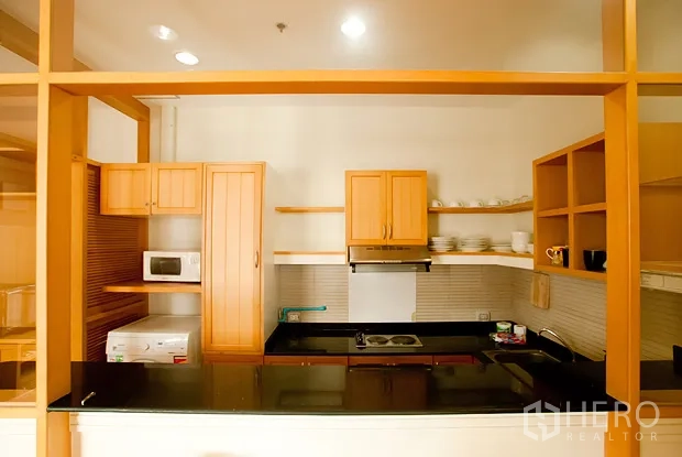 公寓 出租在Khlong Toei, Bangkok - 开放式厨房，木质橱柜与黑色花岗岩台面，配灶台和微波炉。