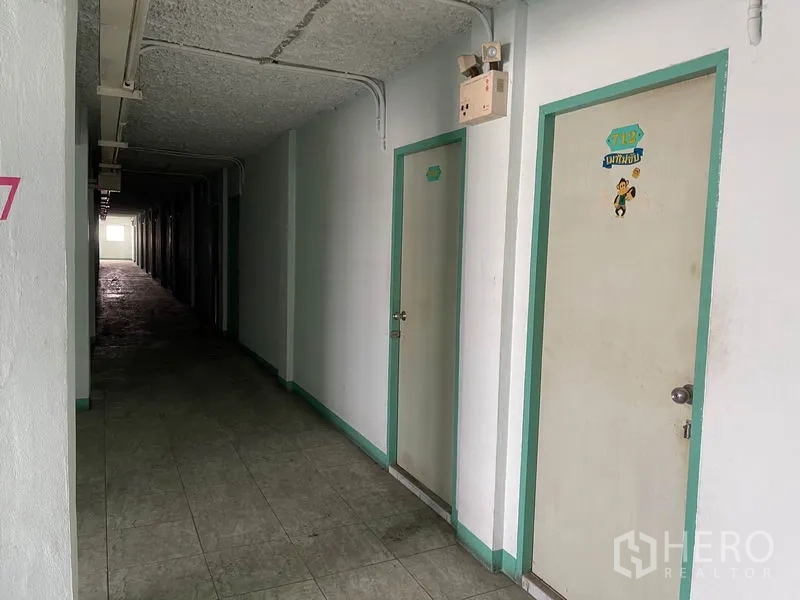 Apartment for sale in Mueang Samut Prakan, Samut Prakan - Dim corridor lined with white unit doors and exposed ceiling conduits.