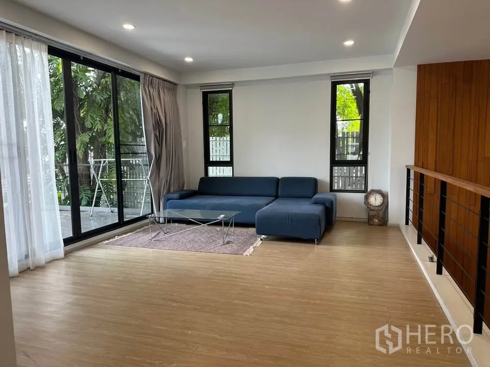 Detached House for sale in Watthana, Bangkok - Lounge area with a blue sectional sofa beside balcony doors.