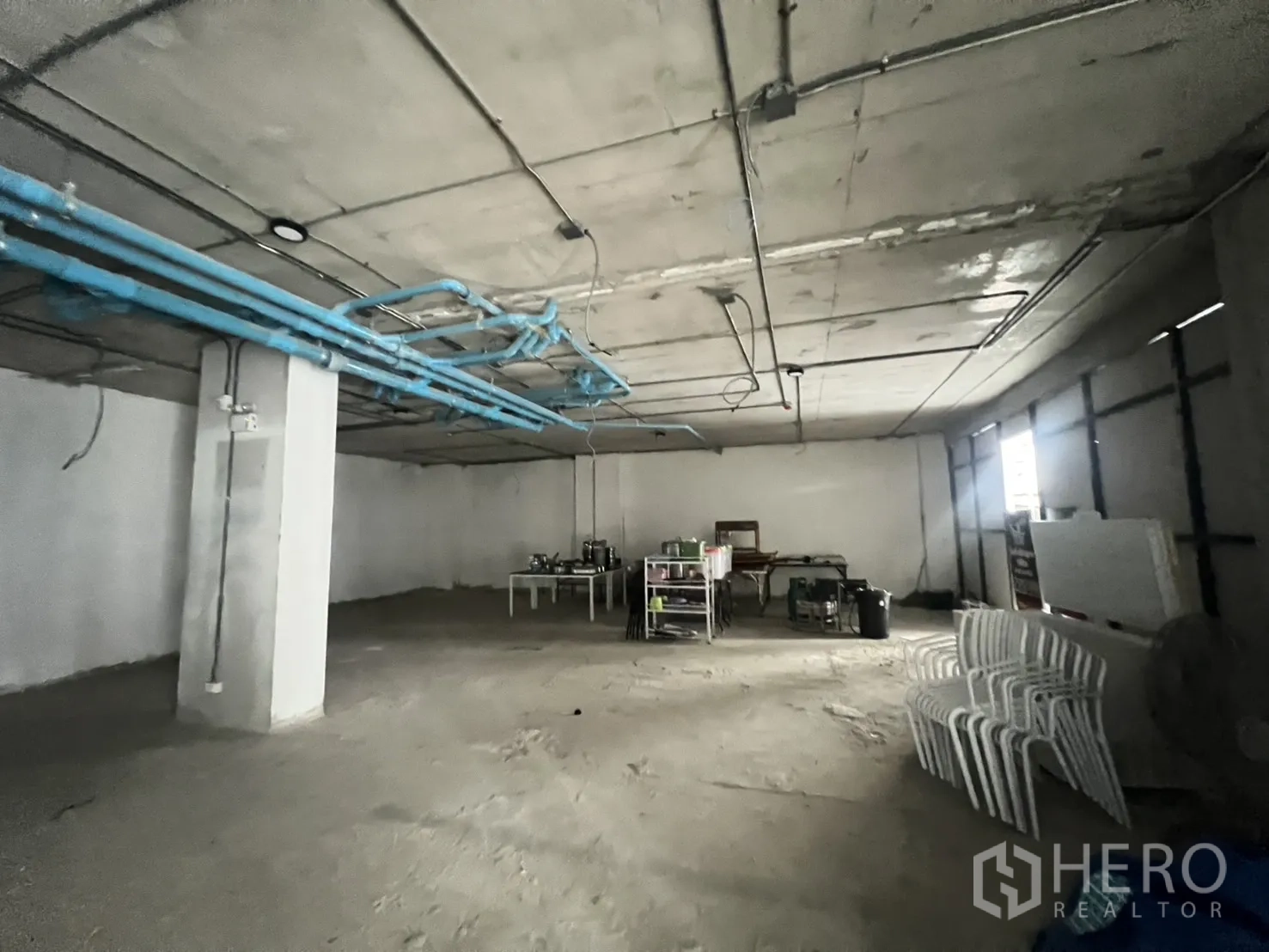 พื้นที่ขายปลีก ให้เช่า - แปลนเปิดโล่งด้านหลังบ้าน เห็นท่อประปาสีฟ้าและเพดานคอนกรีตในยูนิตสภาพเปล่า