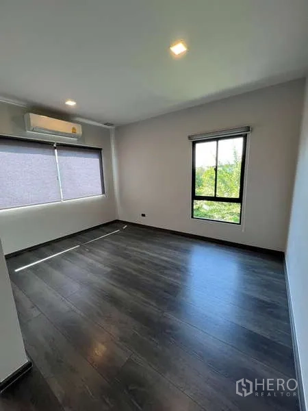 Detached House for rent or sale in Bang Phli, Samut Prakan - Bright bedroom with dark wood flooring, air conditioning and leafy views from the windows.