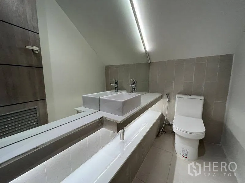联排别墅 for rent in Phra Khanong, Bangkok - 浴室内设双方形台盆、长镜与马桶，天花微斜。
