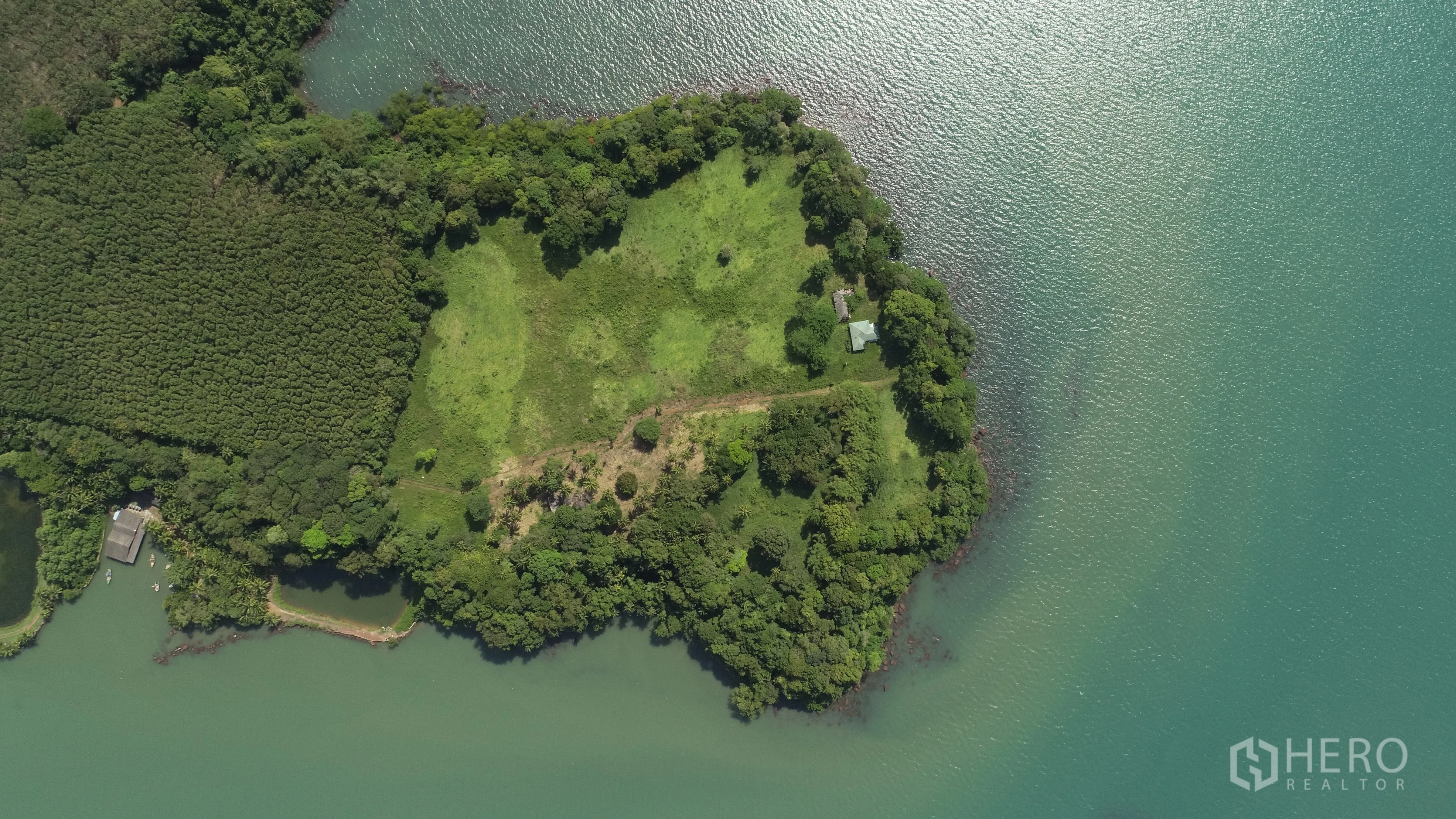 Land for sale in Khlong Toei, Bangkok - Top-down drone shot of grassy waterfront land bordered by dense trees and calm bay waters.
