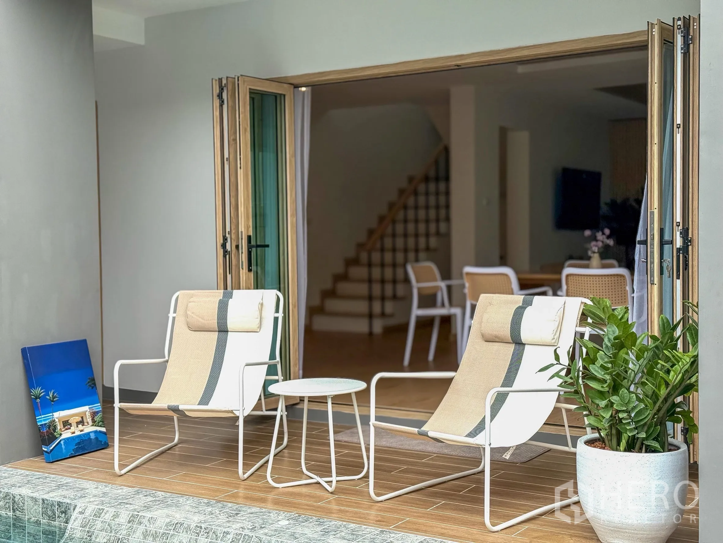 独立式住宅 出售在Suan Luang, Bangkok - 泳池畔露台，两把休闲椅与通往客厅的折叠大门。