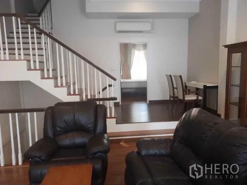 Detached House for rent in Wang Thonglang, Bangkok - Living room with black leather sofas, split-level floor, and staircase to upper level.