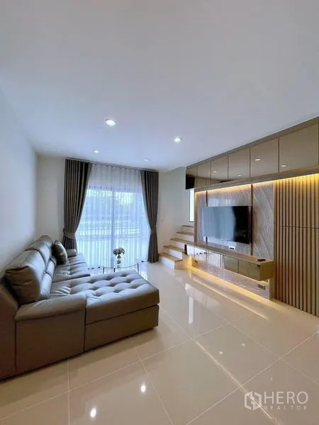 Townhouse for rent in Bang Phli, Samut Prakan - Living area with sectional sofa, TV cabinetry and stairs to upper floor.