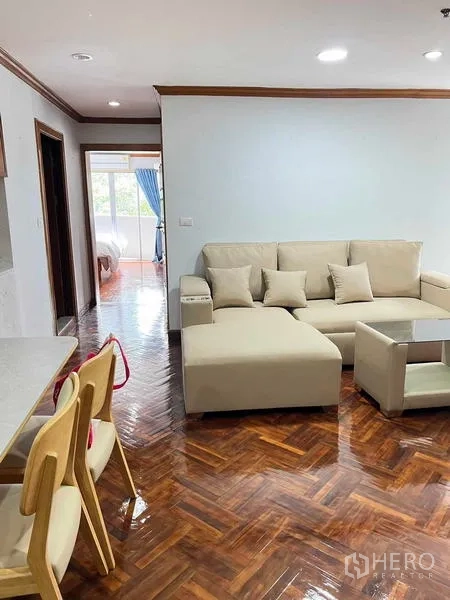 Condominium for rent in Ratchathewi, Bangkok - Open-plan lounge and dining area with herringbone wood flooring leading toward a bedroom with blue curtains.