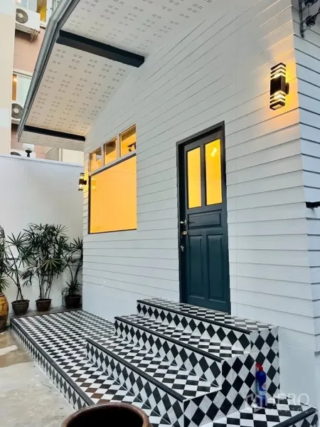 บ้าน ให้เช่า - ภาพระยะใกล้ของทางเข้าพร้อมไฟกิ่ง หน้าต่างบานใหญ่ และบันไดกระเบื้องขาวดำ