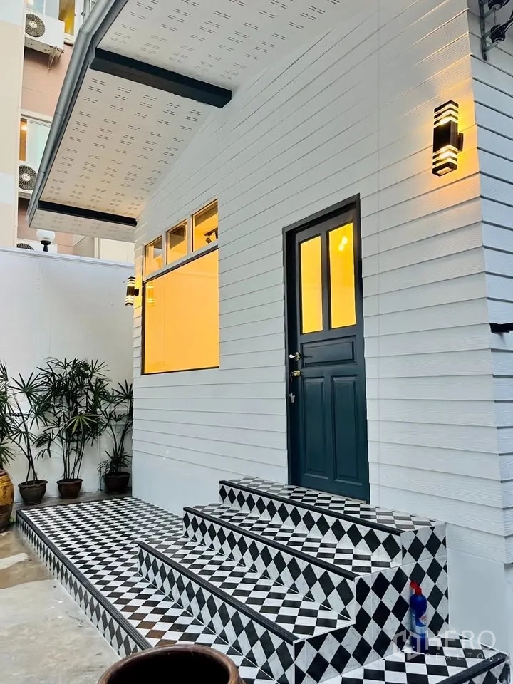 บ้าน ให้เช่า - ภาพระยะใกล้ของทางเข้าพร้อมไฟกิ่ง หน้าต่างบานใหญ่ และบันไดกระเบื้องขาวดำ
