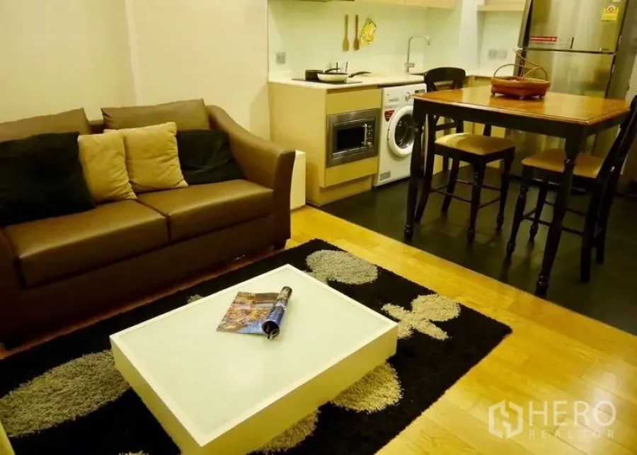 公寓 出售在Watthana, Bangkok - 开放式客厅，皮沙发、茶几与带嵌入式电器的简洁厨房和餐桌。