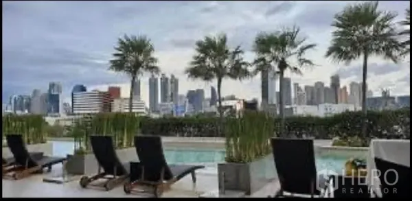 公寓 出租在Sathon, Bangkok - 屋顶泳池配躺椅与棕榈树，远眺曼谷天际线。