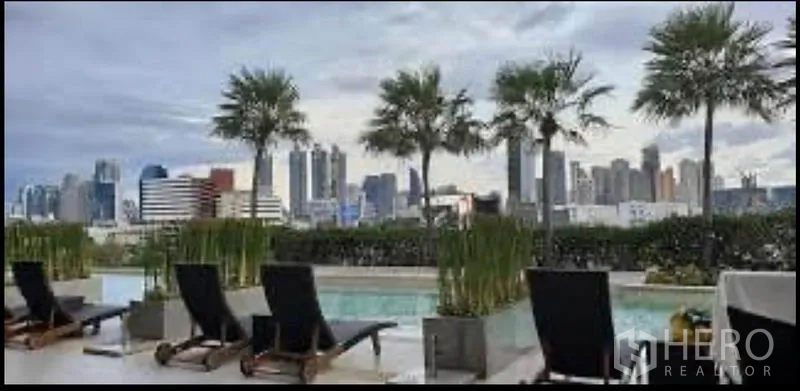 公寓 出租在Sathon, Bangkok - 屋顶泳池配躺椅与棕榈树，远眺曼谷天际线。