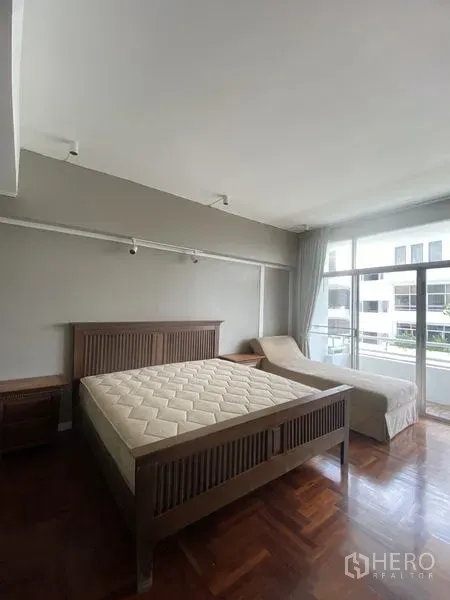 公寓 出租在Sathon, Bangkok - 采光充足的主卧，木质床与贵妃椅，拼花木地板，落地窗通往阳台。