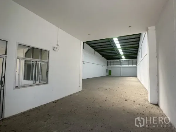 Warehouse for rent in Pathum Thani - Spacious warehouse interior with white walls, office partition and high metal roof with skylights.