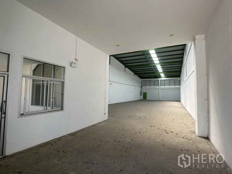 Warehouse for rent in Pathum Thani - Spacious warehouse interior with white walls, office partition and high metal roof with skylights.