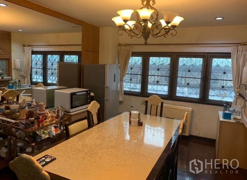 Detached House for sale in Khlong San, Bangkok - Dining area with a long stone-top table, chandelier and wide windows.