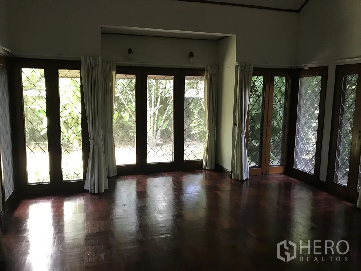 Detached House for rent in Khlong Toei, Bangkok - Bright room with floor-to-ceiling windows, garden views, and polished wood flooring.