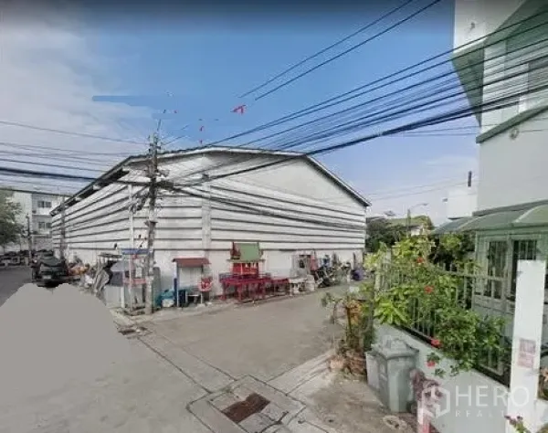 货栈 出租在Prawet, Bangkok - 曼谷Prawet区安静小巷中的白色山墙屋顶仓库外观，可见电线与邻近民宅。