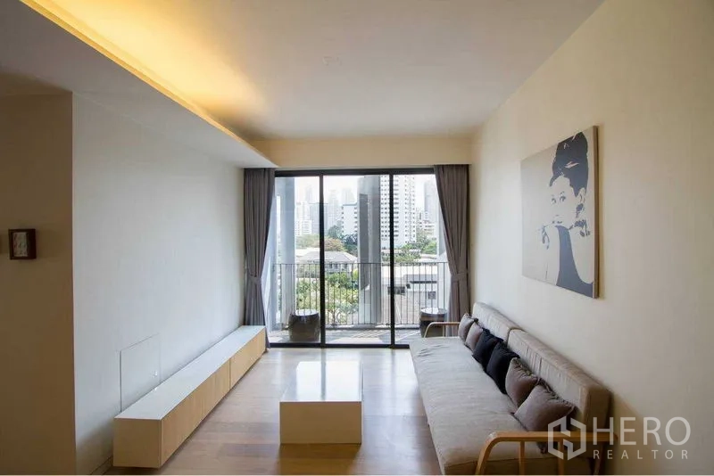 คอนโด ให้เช่าหรือขายในWatthana, Bangkok - ห้องนั่งเล่นสว่างพร้อมประตูกระจกเต็มบานเปิดสู่ระเบียงวิวเมือง โซฟามินิมอล พื้นไม้ ตู้วางของบิวท์อิน และภาพศิลปะบนผนัง