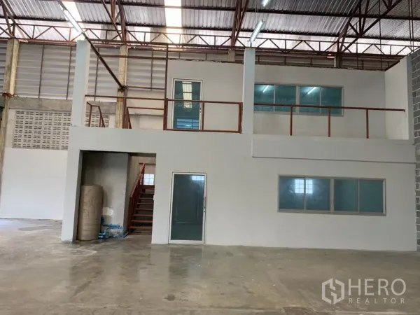 Warehouse for rent in Min Buri, Bangkok - Interior of a warehouse showing a mezzanine office with glass windows under a high steel truss roof.