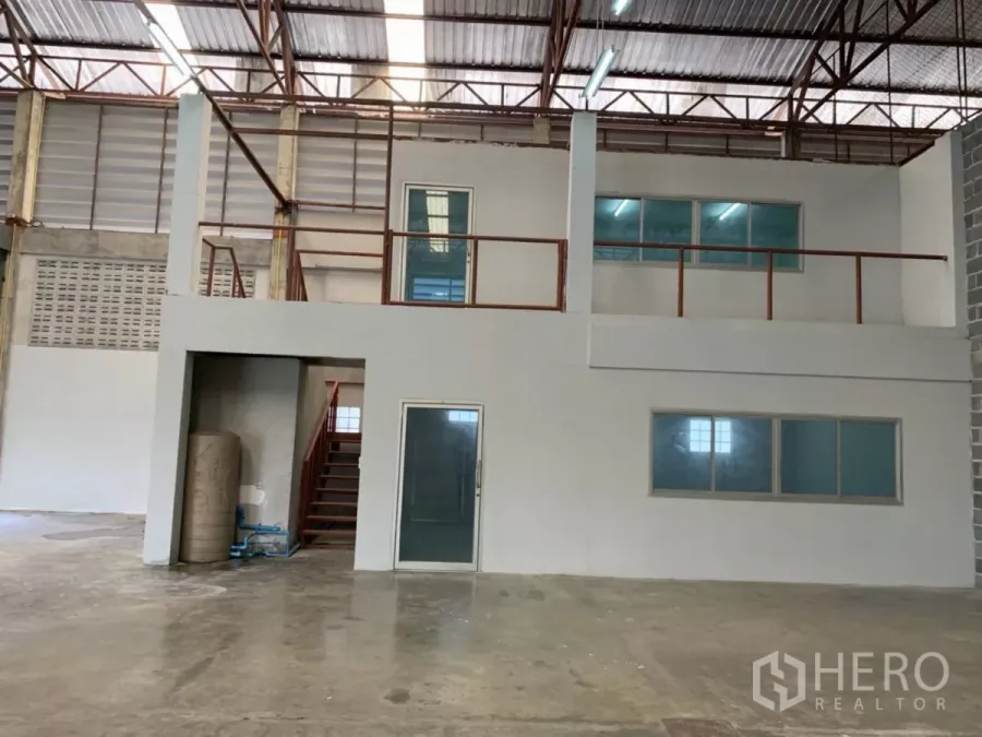 Warehouse for rent in Min Buri, Bangkok - Interior of a warehouse showing a mezzanine office with glass windows under a high steel truss roof.