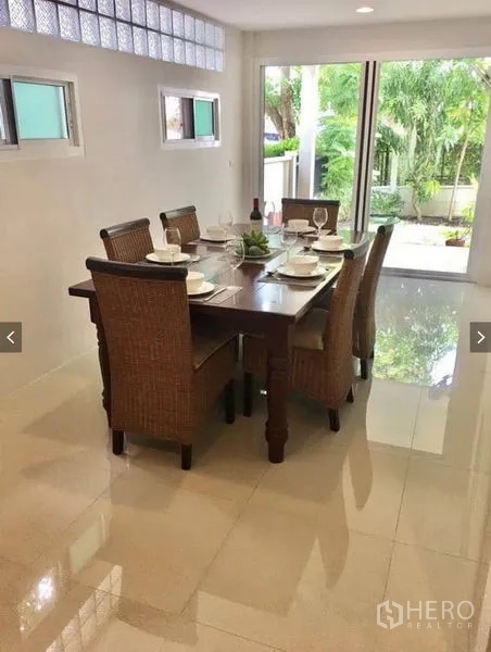 Townhouse for rent or sale in Suan Luang, Bangkok - Dining area with six-seat wooden table and rattan chairs opening to the garden via glass doors.