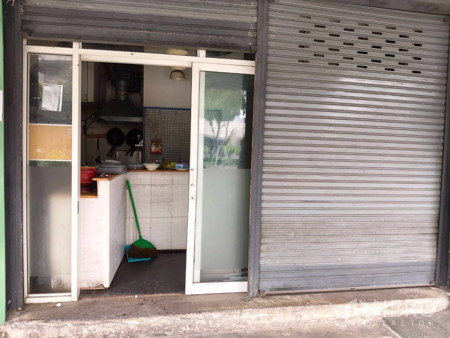 Retail Space for rent in Sathon, Bangkok - Storefront with glass door, metal roll-up shutter, and a small tiled kitchen area with an exhaust hood.